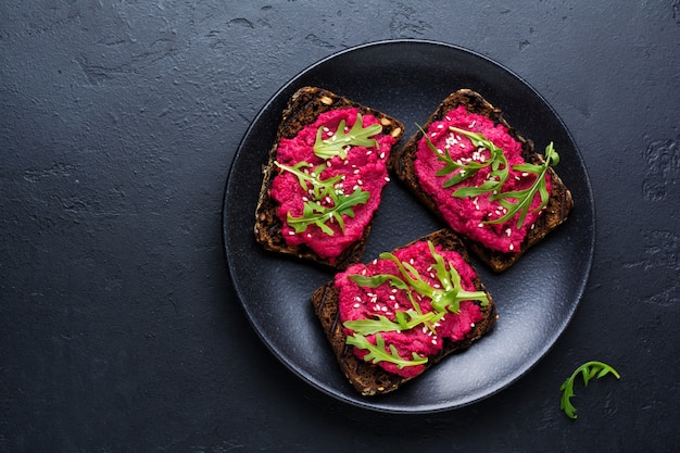 Bruschetta with beetroot hummus, arugula and sesame seeds on dark concrete surface