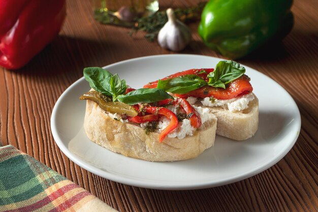 Bruschetta with bell pepper, basil, pesto sauce and mozzarella on a white plate on a wooden background.