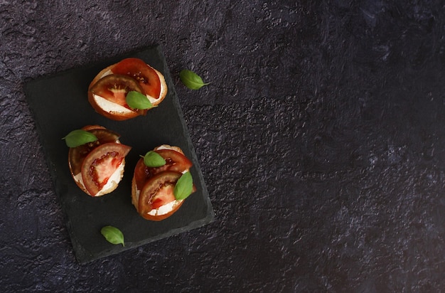 Bruschetta with cheese and red and black tomatoes with basil on a dark background