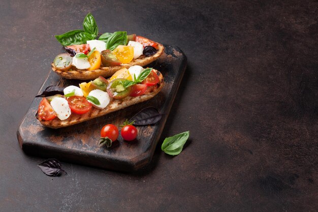 Photo bruschetta with cherry tomatoes, mozzarella and basil on wooden board. caprese salad. with copy space