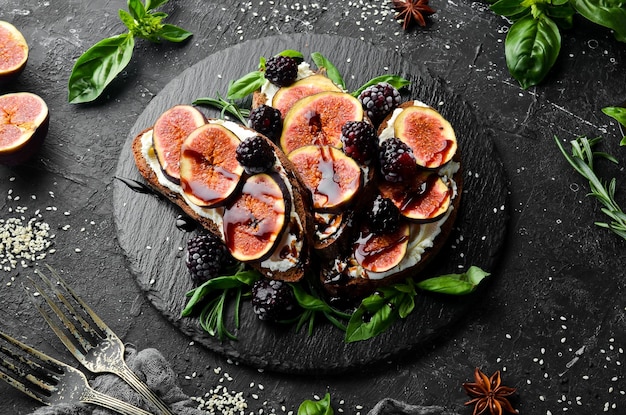 Bruschetta with Philadelphia cheese figs and blackberries on a black stone plate Top view Free space for your text