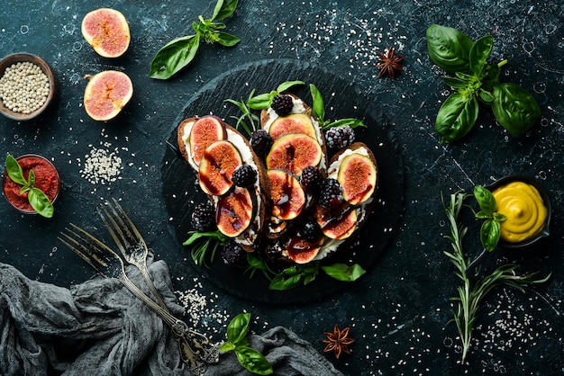 Bruschetta with Philadelphia cheese figs and blackberries on a black stone plate Top view Free space for your text