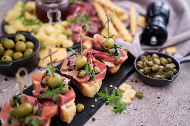 Bruschetta with prosciutto ham and capers with traditional antipasto meat plate on background