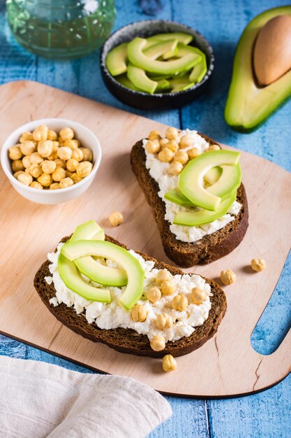 Bruschetta with ricotta avocado and chickpeas on rye toast on a board Healthy food Vertical view