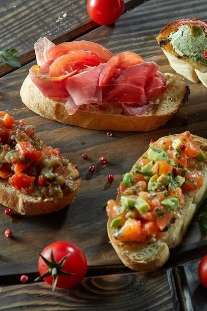 Bruschetta with roasted tomatoes, avocado, salmon, ham, peppers, herb on a wood board