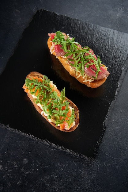 Bruschetta with salmon,cherry tomatoes,fresh arugula and cream cheese on plate on Dark grey black slate background