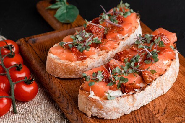 Bruschetta with salmon, dried tomatoes, herbs, cottage cheese, on a concrete background, wooden board