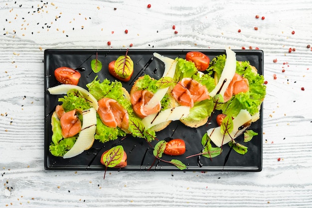 Bruschetta with salmon, lettuce and parmesan cheese on a black plate. Top view. Rustic style.