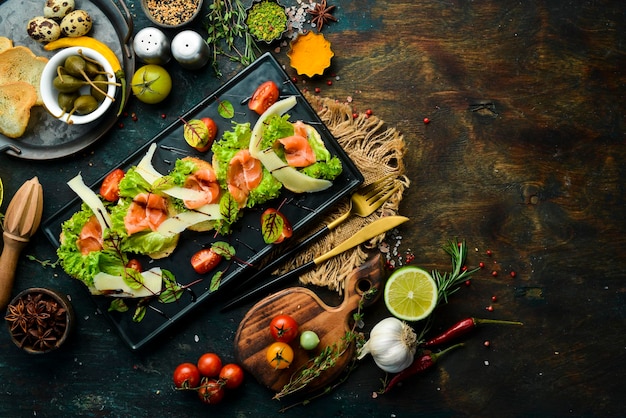 Bruschetta with salmon lettuce and parmesan cheese on a black plate Top view Rustic style