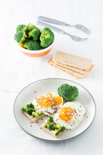 Bruschetta con uova strapazzate e broccoli su un pane croccante di cereali con semi di sesamo e semi di lino su un piatto sul tavolo. vista verticale
