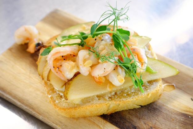 Bruschetta with shrimp pear and pine nuts on a wooden board Horizontal photo