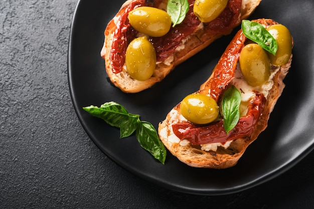 Bruschetta with sun dried tomatoes Toast or sandwich with ricotta sun dried tomatoes and Provence herbs with basil servered on black plate on black background table Selective focus