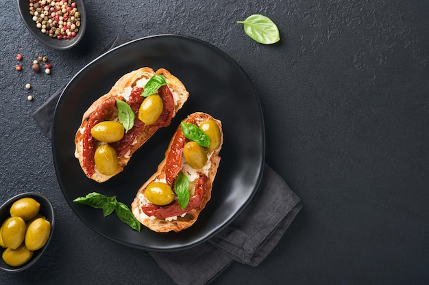 Bruschetta con pomodori secchi toast o panino con ricotta pomodori secchi ed erbe di provenza con basilico servito su piatto nero su sfondo nero tavolo banner menu vista dall'alto ricetta