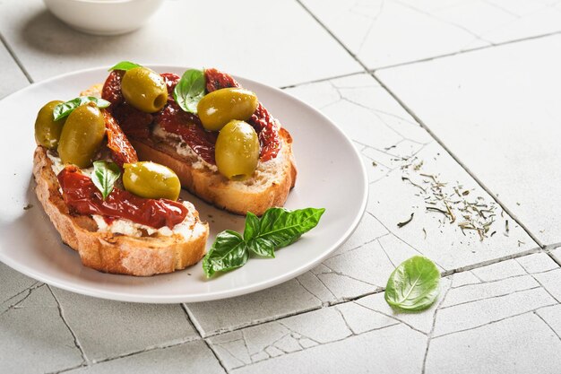 Bruschetta with sun dried tomatoes Toast or sandwich with ricotta sun dried tomatoes and Provence herbs with basil servered on a plate on a grey old cracked tile table Top view banner menu recipe