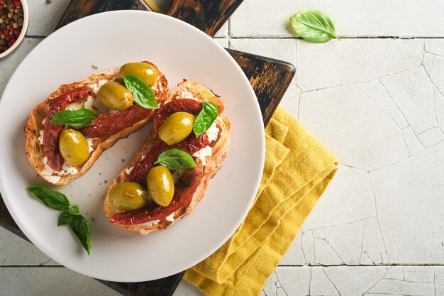 Bruschetta with sun dried tomatoes toast or sandwich with\
ricotta sun dried tomatoes and provence herbs with basil servered\
on a plate on a grey old cracked tile table top view banner menu\
recipe