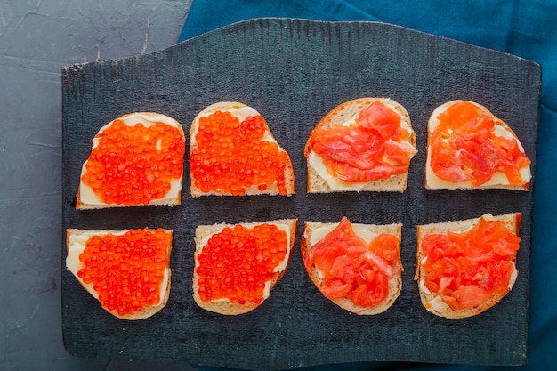 Bruschetta with trout and red caviar on a black board.