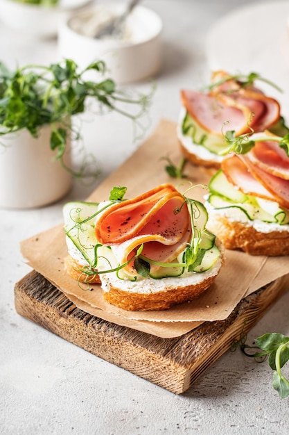 Bruschettas with baguette meat cream cheese microgreenery cucumber in composition on wooden board