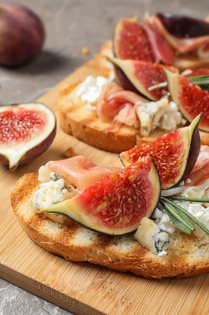 Bruschettas with cheese prosciutto and figs served on wooden board closeup