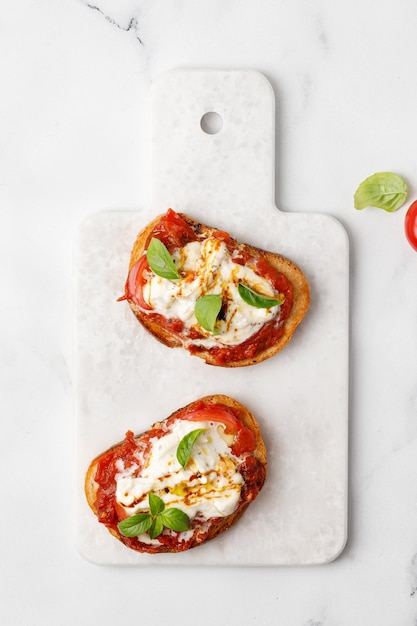 Bruschettas with stracciatella cheese cherry tomatoes and basil on marble board top view