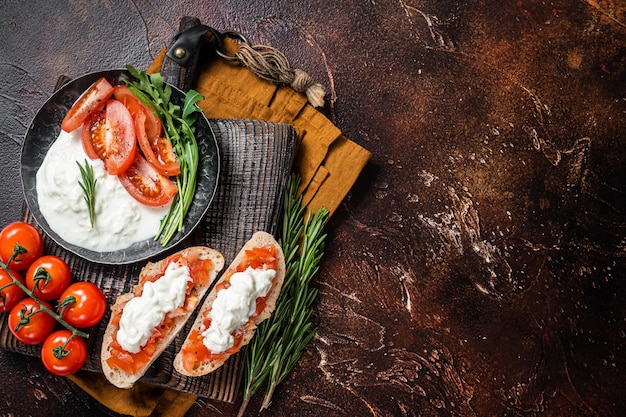 Bruschettas with stracciatella cheese chopped cherry tomatoes and rosemary dark background top view copy space