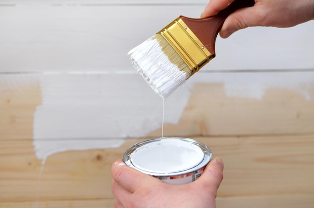 Brush and jar with white paint in hands close-up