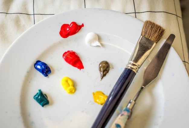 Brush and Metal Squeegee for Painting on a White Dish with Coloured Paint Sticks on a Bed Duvet