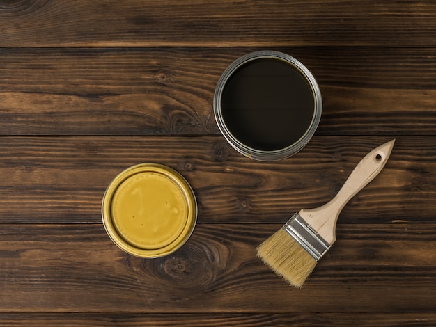 Brush and open iron jar with tinting composition on a wooden surface. The rendering of wood.