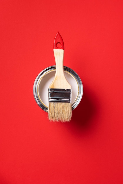 Brush and open paint can on trendy red background Top view copy space Appartment renovation repair building and home design concept