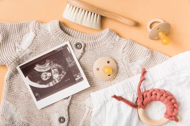 Foto spazzola; ciucci; giocattolo; vestiti del bambino di lana su uno sfondo arancione