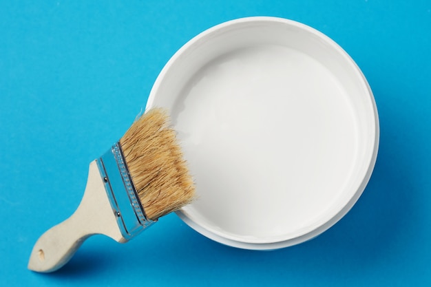 Brush and paint can with white color on a blue background, closeup