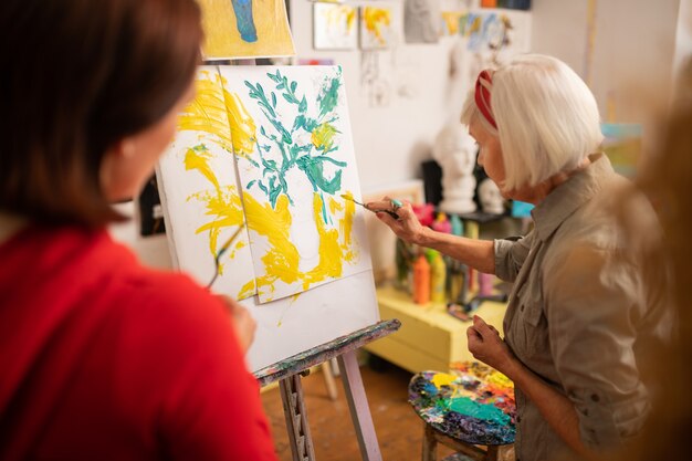 Brush and picture. Aged artist with bob cut holding painting brush and coloring picture