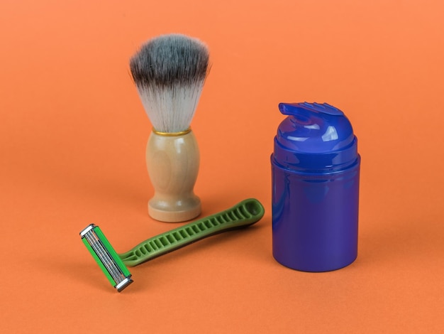 オレンジ色の背景にブラシ、カミソリ、ジェル付きの青いチューブ。男性の衛生の最小限の概念。男性用化粧品の最小限のコンセプト。