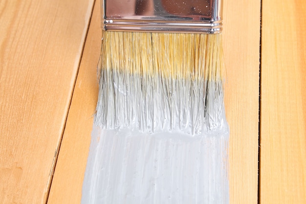 Brush with can paint in hand. A man paints wooden boards in a gray paint brush.