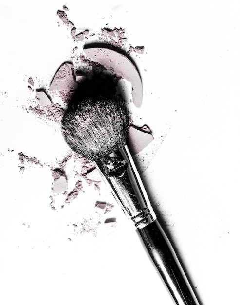 Brush with crushed eyeshadow and powder closeup isolated on white background