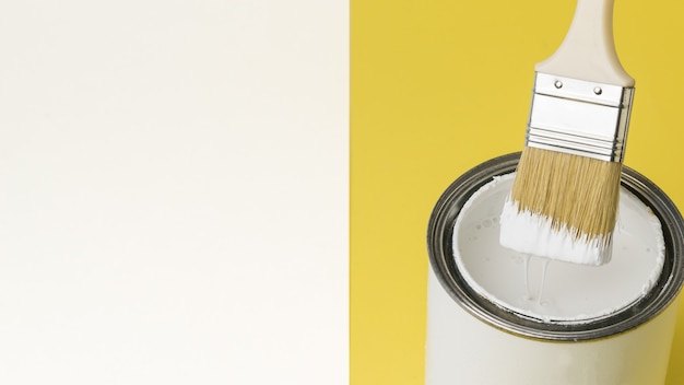 Brush with dripping white paint over a jar on a white and yellow background. Execution of painting works. Place for text.