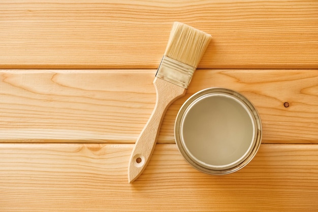 Brush with a jar of paint on a background of natural wooden boards.