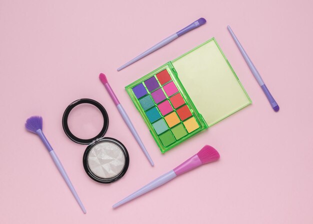 Brushes highlighters and multicolored eye shadow on a light pink background