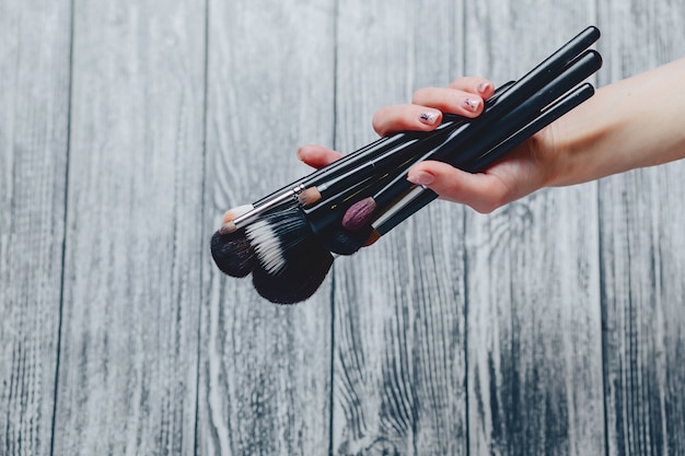 Brushes for makeup in hands on wooden background