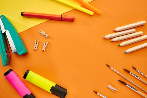 Brushes, markers and stapler closeup on orange background. Office stationery supplies, school or education accessories, writing and drawing tools