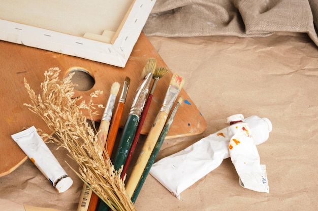 Brushes, paints in tubes, a wooden palette, canvas on a stretcher, paper and linen on a table, an artist's workshop