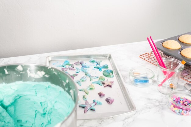 Brushing chocolate mermaid tails with food glitter to decorate vanilla cupcakes.