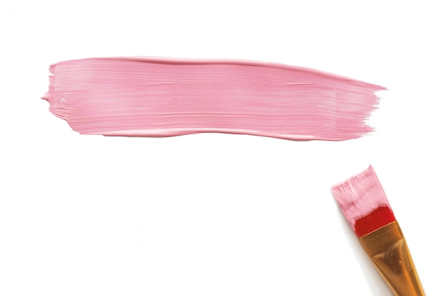 A brushstroke of pink acrylic paint and a paint brush next to it. Isolated