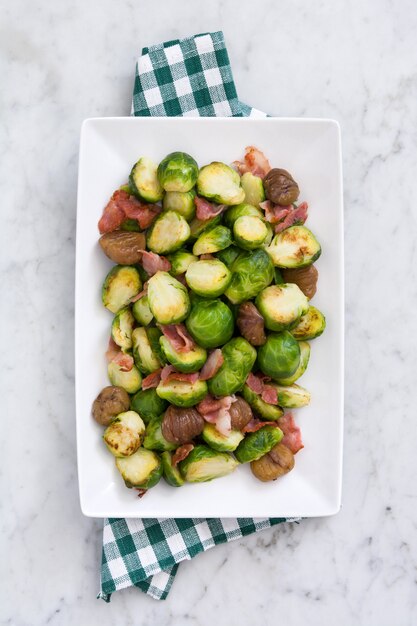 Brussels sprouts with chestnuts and bacon on white marble top view