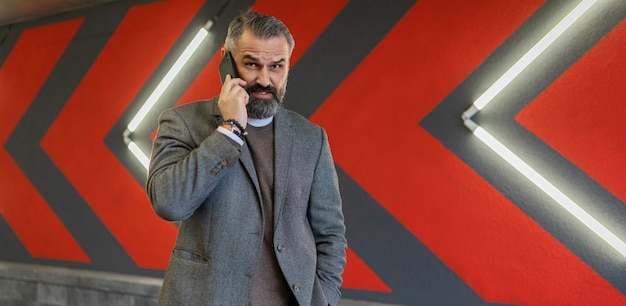 Brutal adult male businessman speaks on a mobile phone against the background of a bright wall with