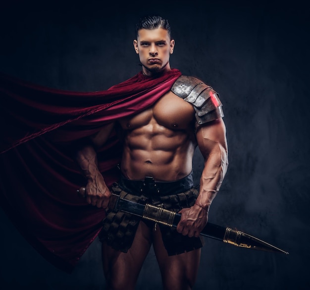 Brutal ancient Greece warrior with a muscular body in battle uniforms posing on a dark background.