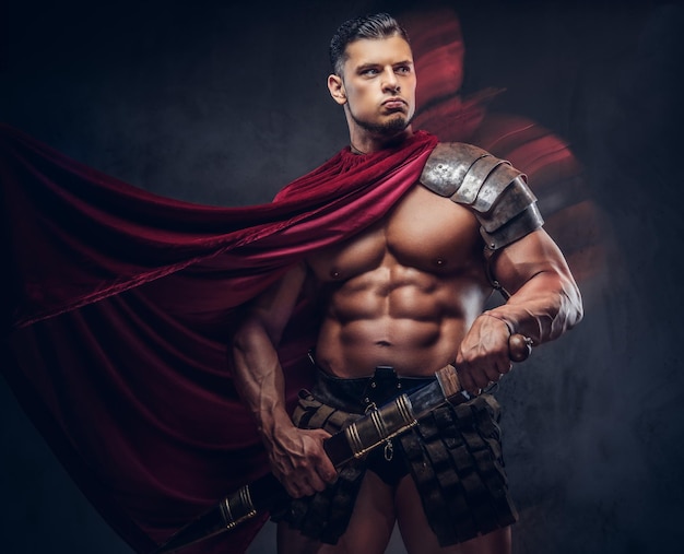 brutal ancient greece warrior with a muscular body in battle uniforms posing on a dark background.