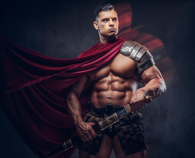 Brutal ancient Greece warrior with a muscular body in battle uniforms posing on a dark background.