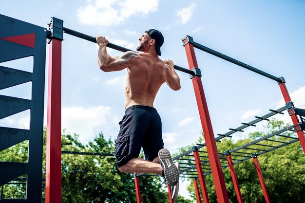 Brutale uomo atletico che fa esercizi di pull-up su una traversa.