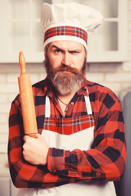 Brutal bearded chef cook in white uniform standing with crossed arms in the kitchen