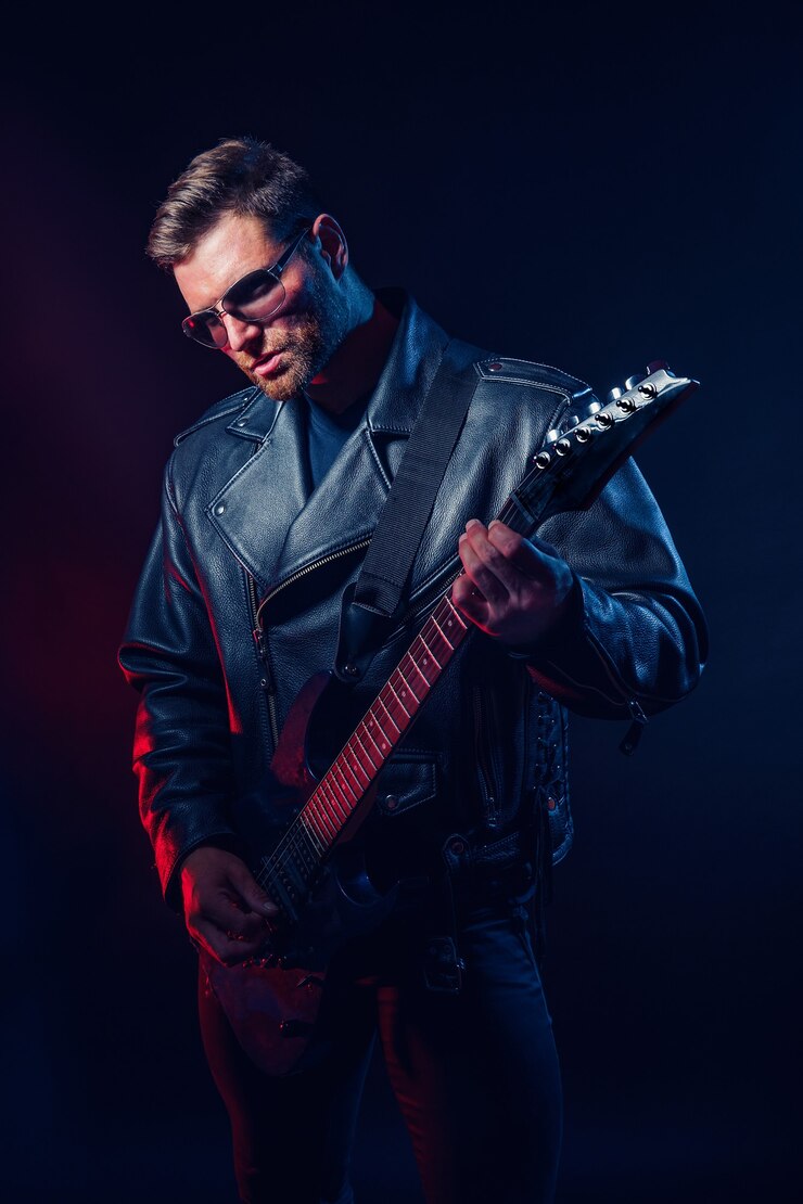 Photo brutal bearded heavy metal musician in leather jacket cap and sunglasses is playing electrical guitar on black 